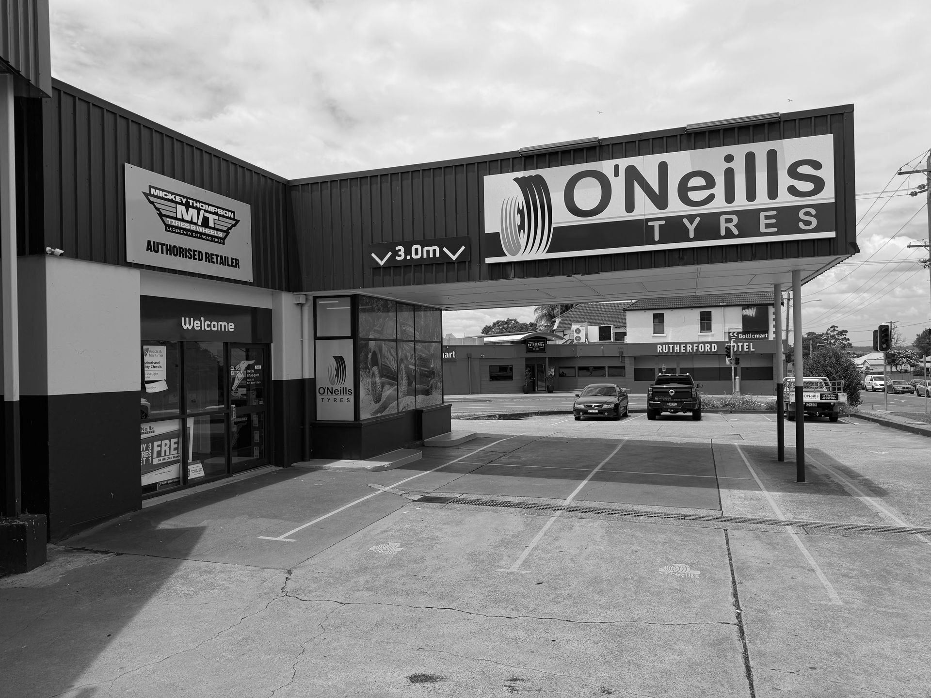 Exterior view of O'Neills Tyres with a yellow and blue facade, parking spots, and a 3.0m clearance sign.