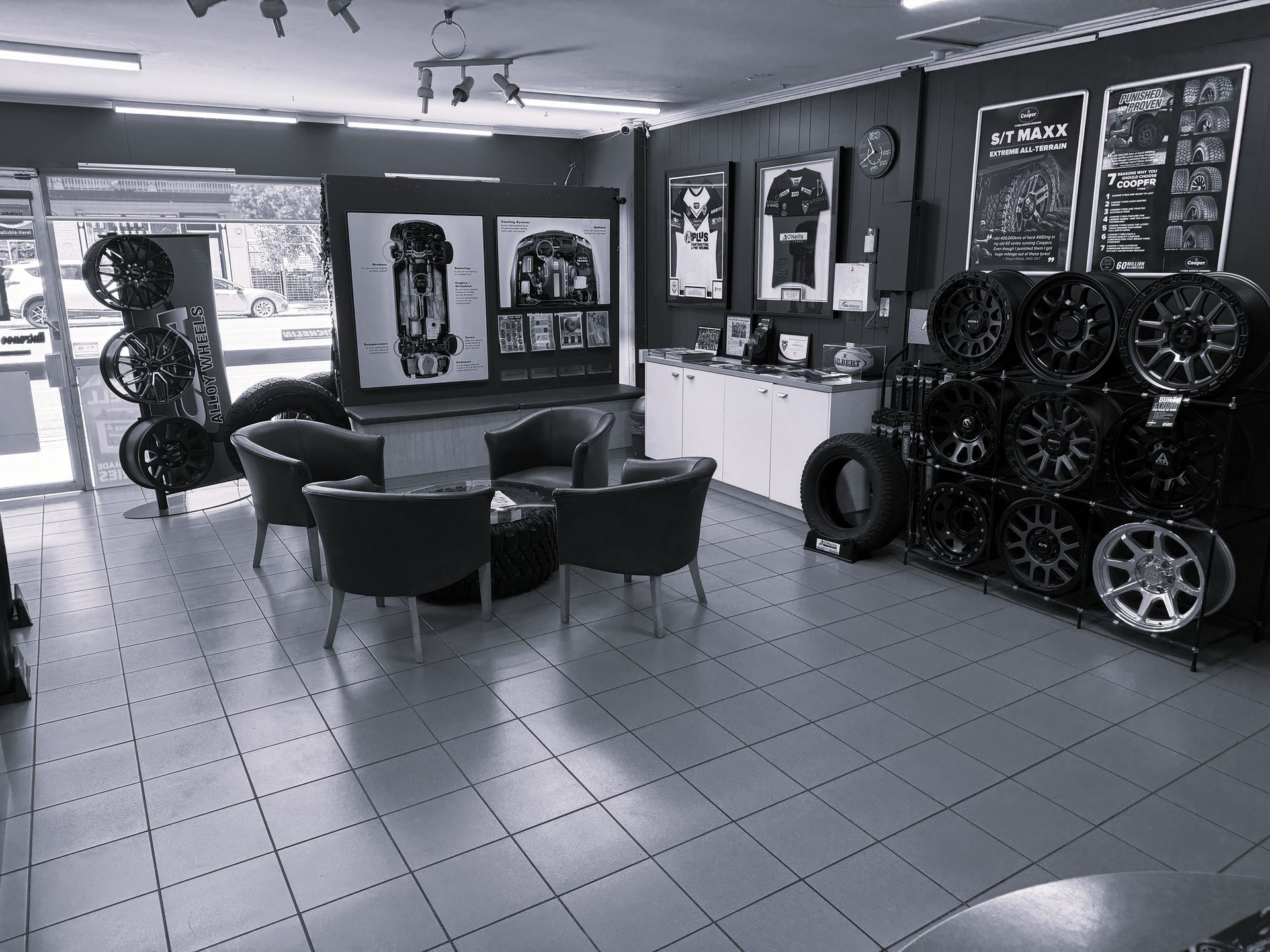 A tire and wheel shop featuring a lounge area with armchairs, display racks of various rims, and automotive wall art.