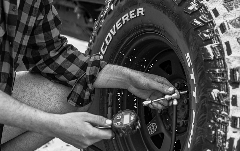A person in a plaid shirt uses a digital tire pressure gauge to check the pressure of an off-road vehicle tire.