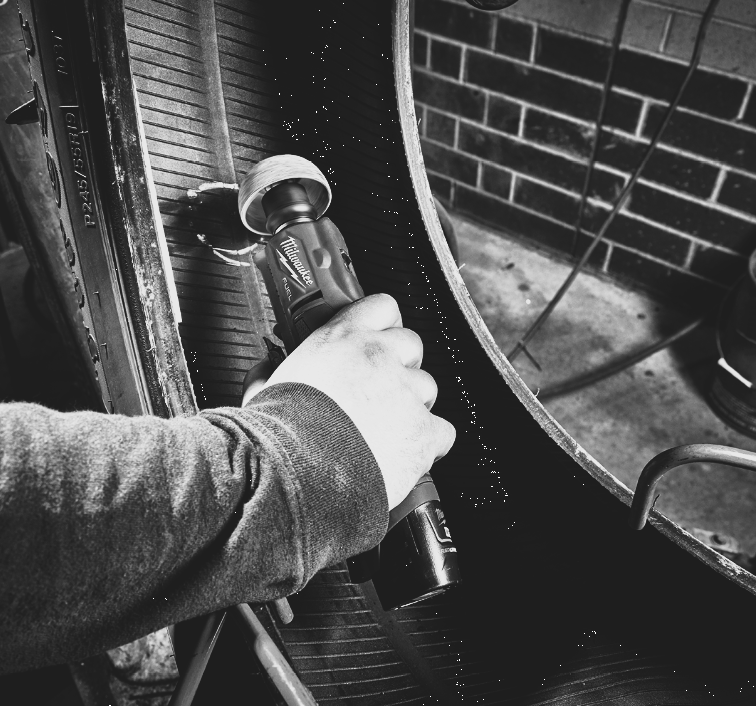 A hand uses a power buffer to buff the inside of a tire in a workshop.