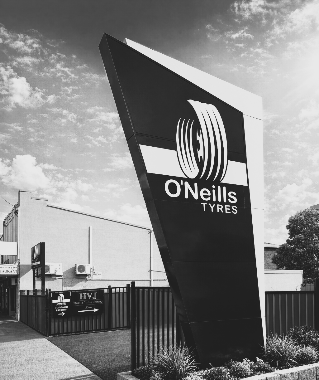 A tall, angled O'Neills Tyres sign stands outside a building on a bright day.