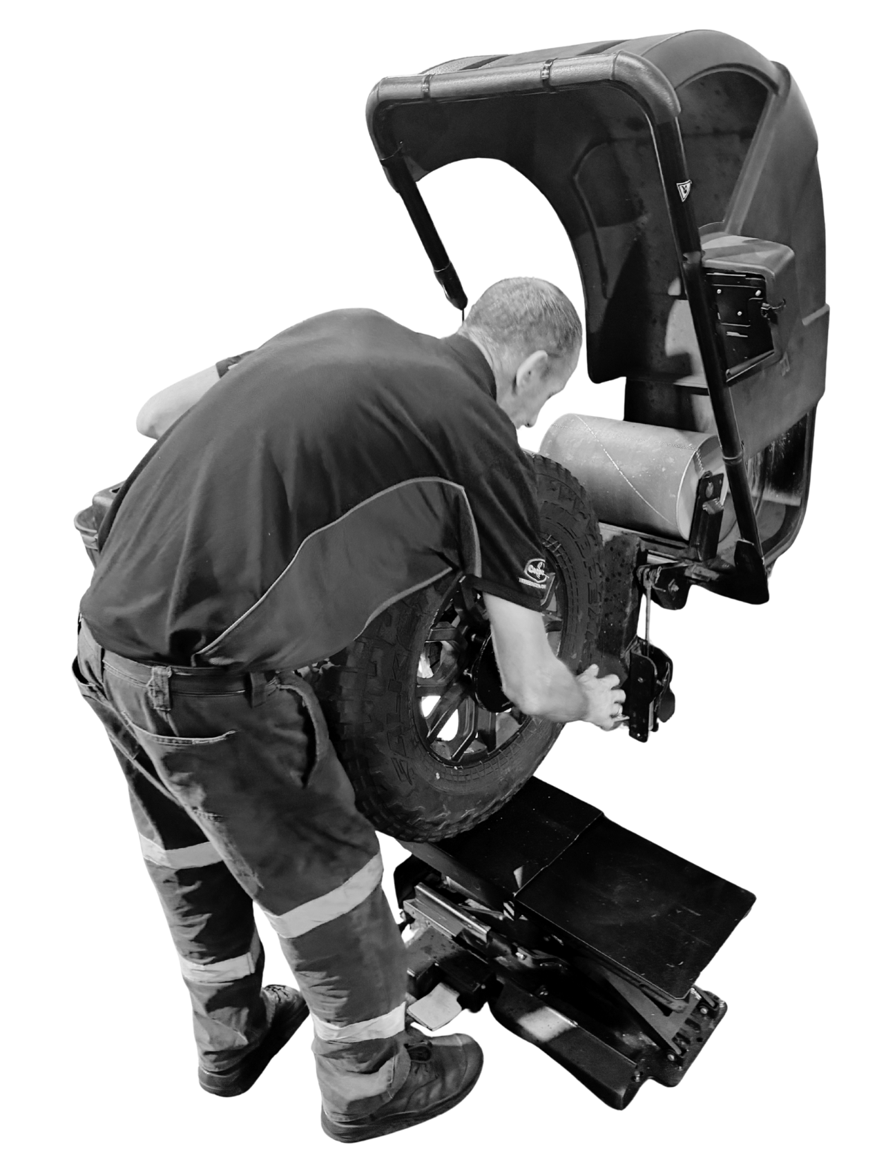A person wearing work clothes operates a tire balancing machine in a shop setting.