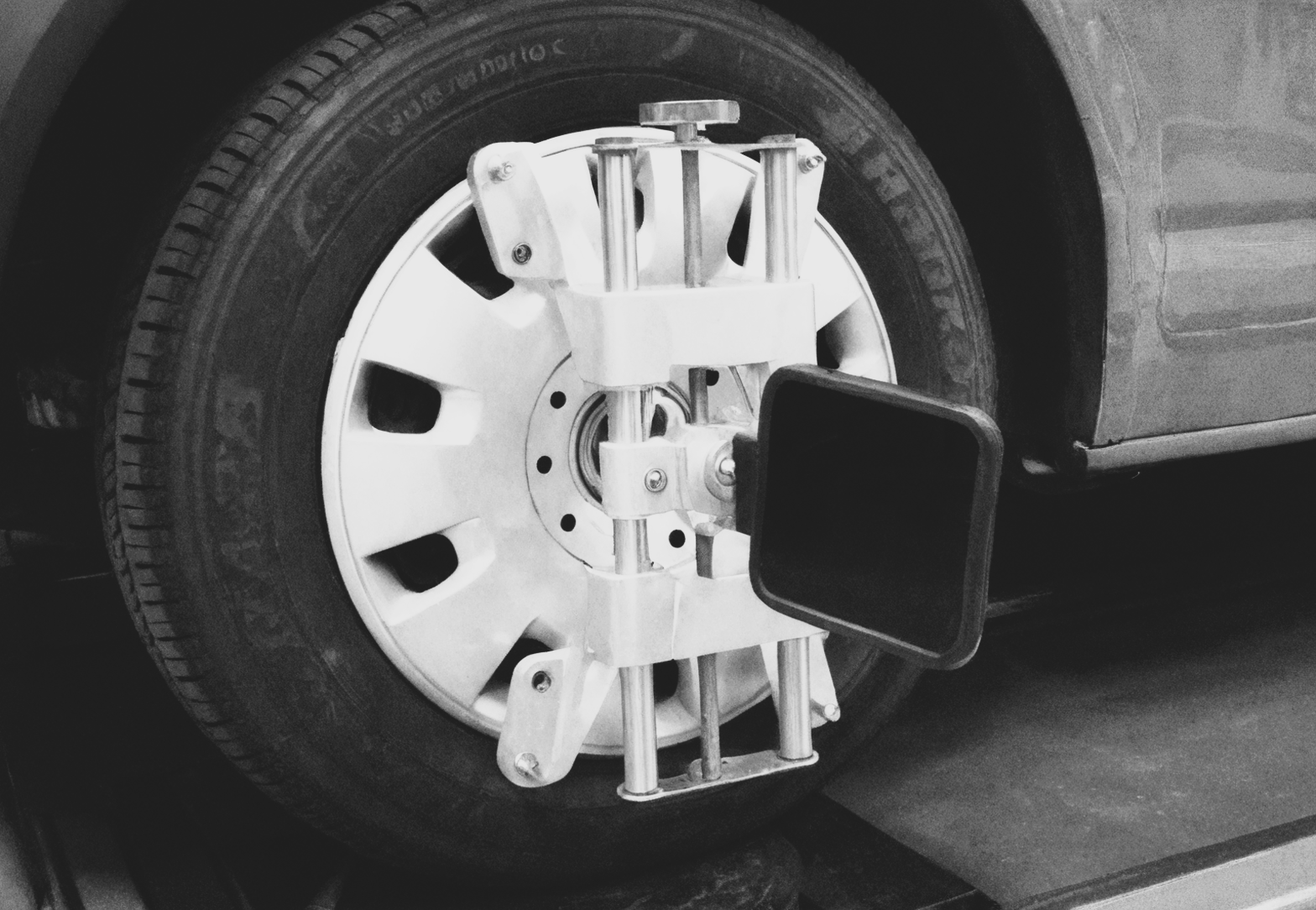 A wheel alignment sensor clamped onto a car tire for diagnostic testing in an automotive workshop.