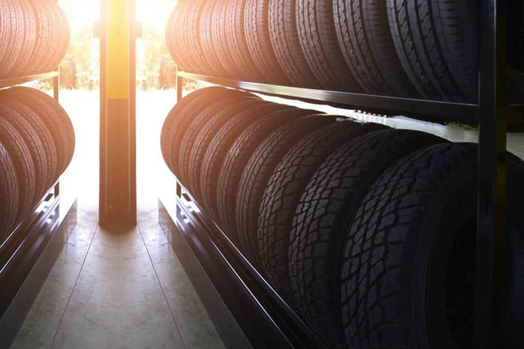 Tires stacked neatly on metal shelving in a garage with bright sunlight visible in the background.
