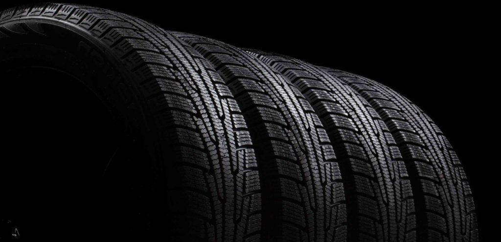 A close-up, dark-themed shot of several black tires lined up, showing the detailed tread patterns on their surfaces.