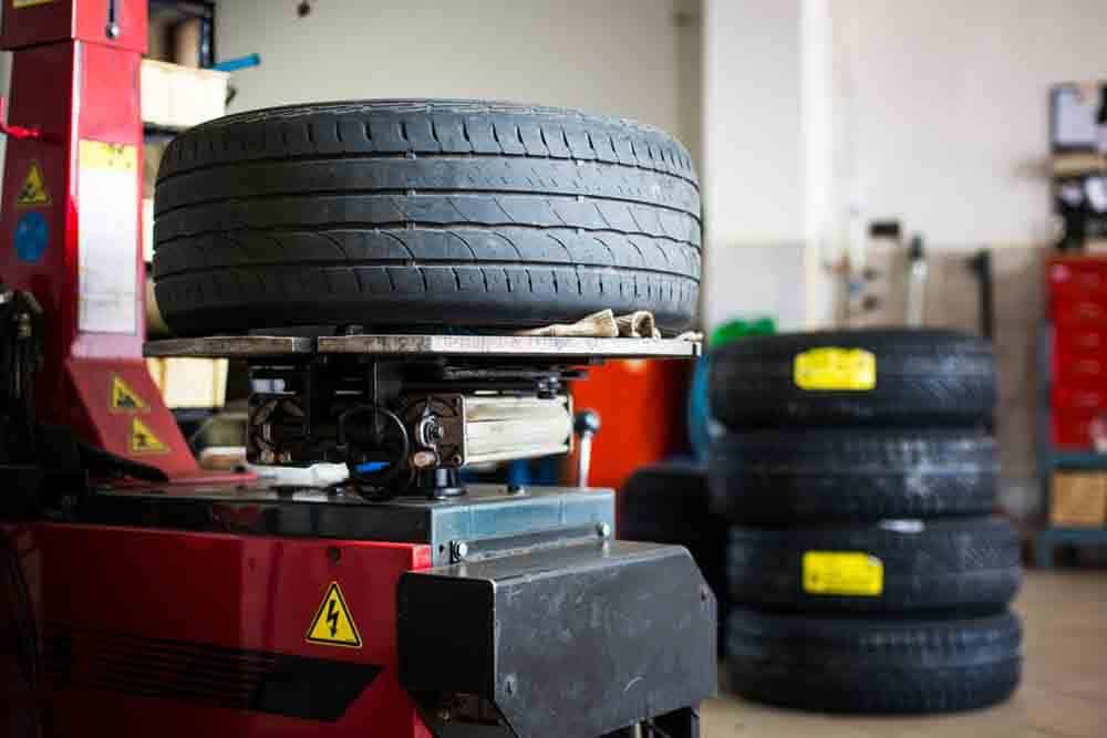 A tire on a red tire changing machine, with a stack of tires in the background of an auto repair shop.