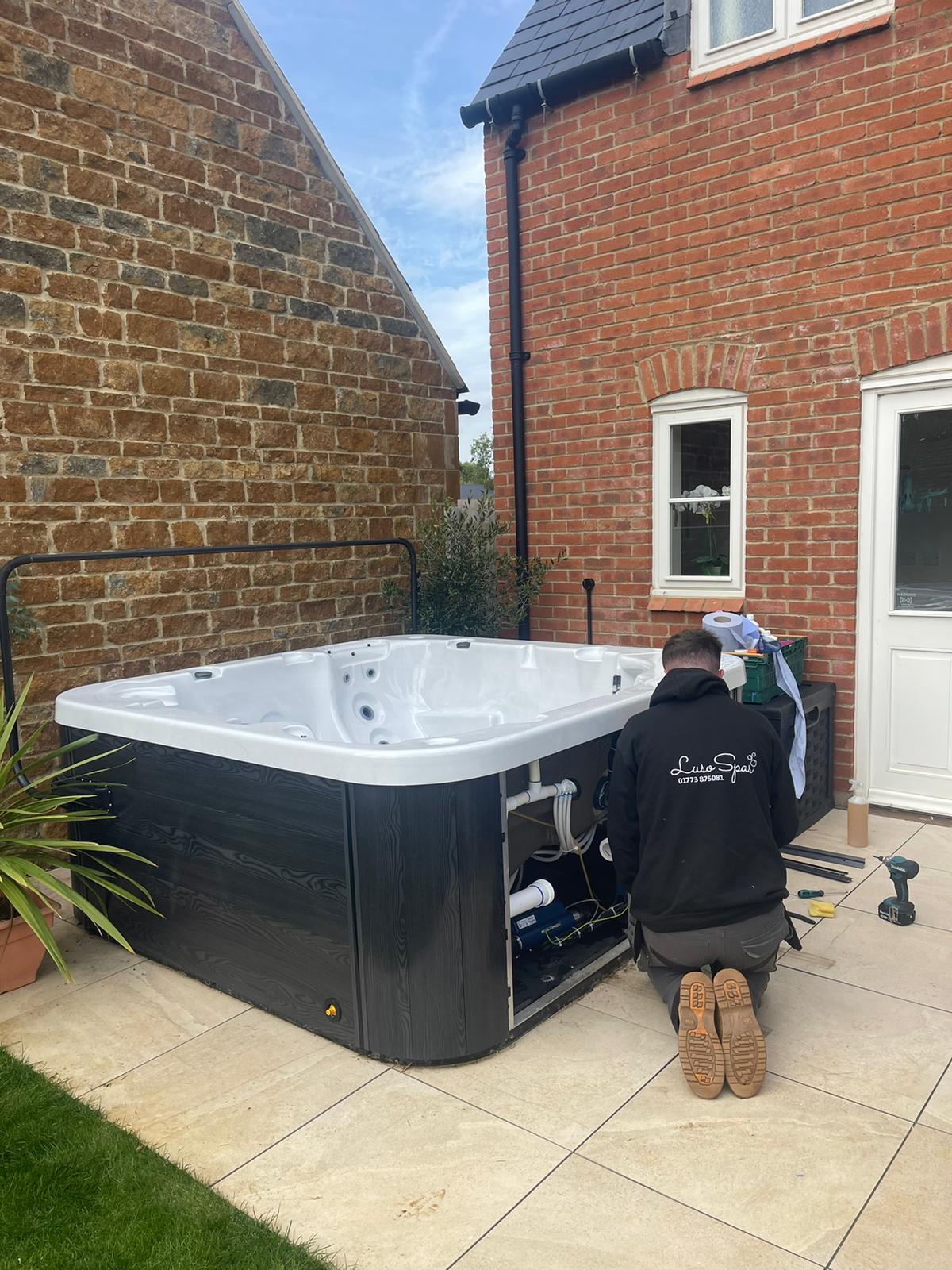 A man is working on a hot tub outside of a brick house.