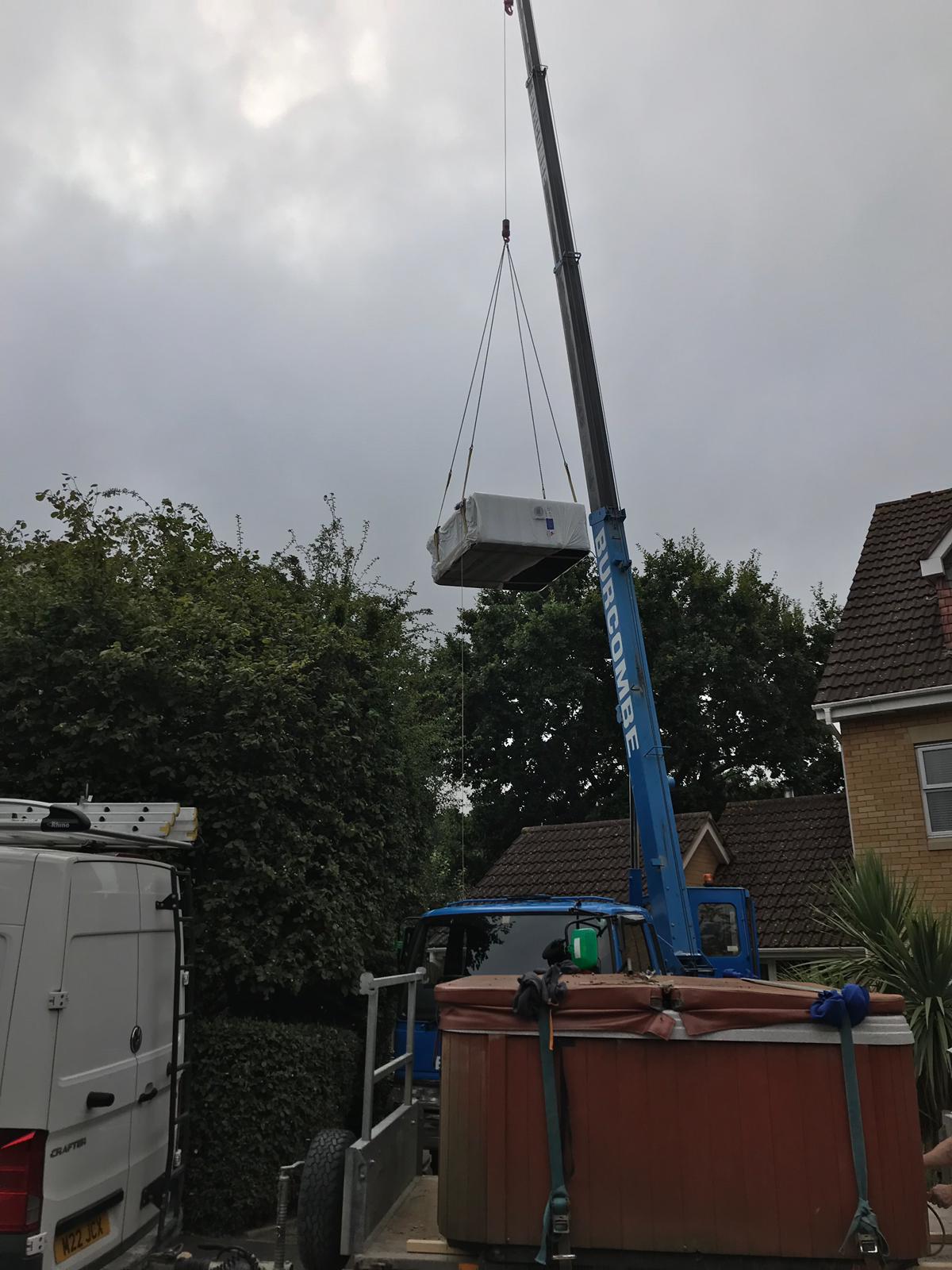 A hot tub is being lifted by a crane in front of a house