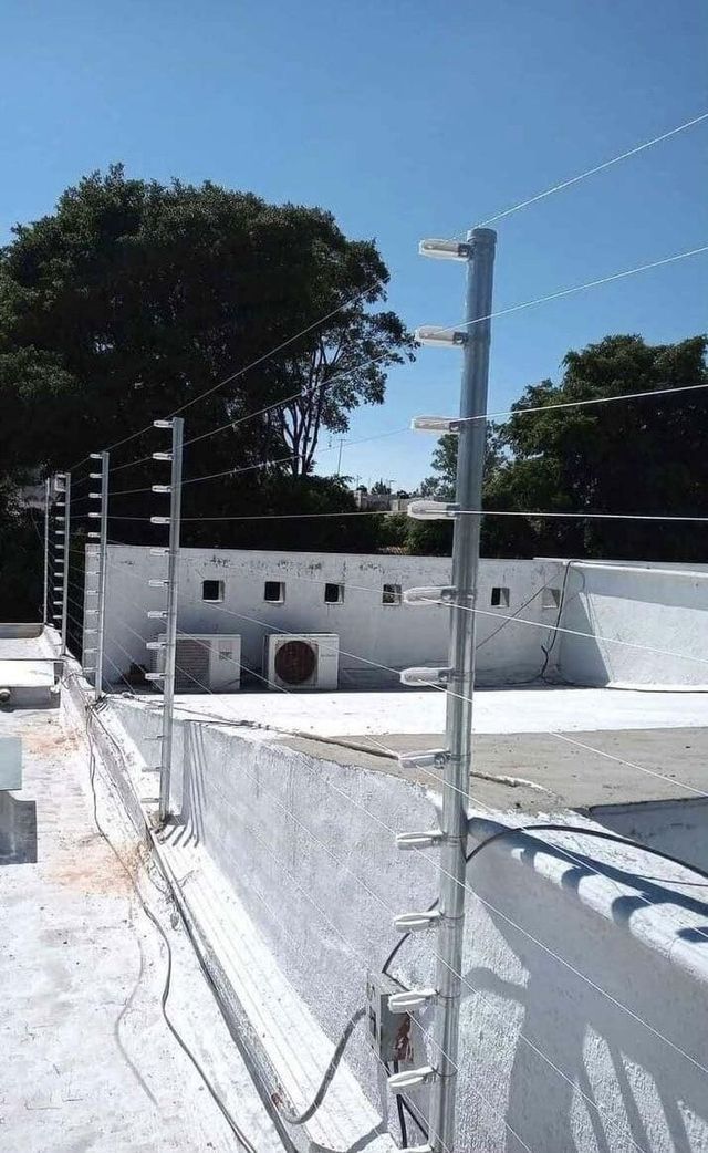 Un edificio blanco con una valla alrededor y una piscina al fondo.
