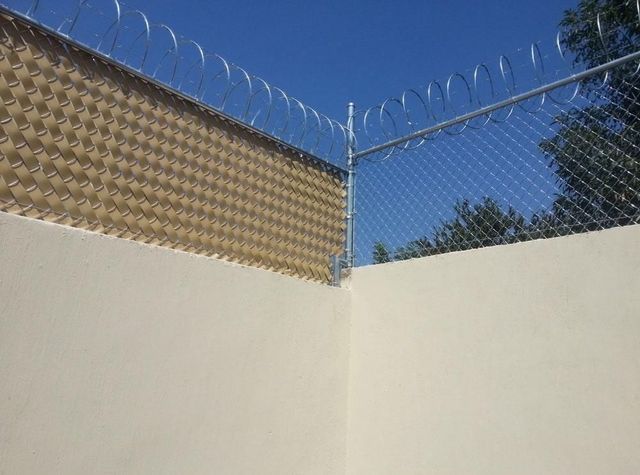 Una valla de tela metálica con alambre de púas encima de una pared blanca.