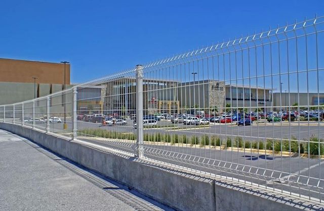 Una valla blanca rodea un aparcamiento con un edificio al fondo.