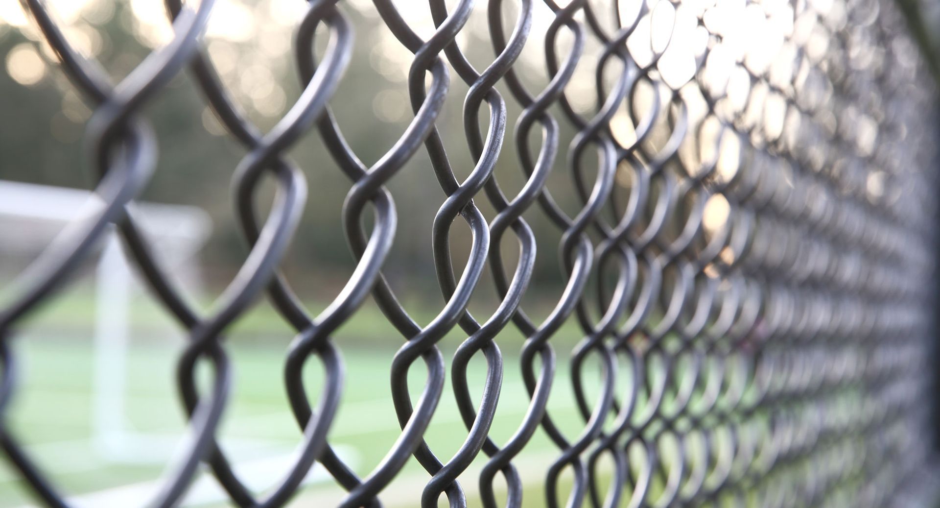 Un primer plano de una valla metálica con una cancha de tenis al fondo.