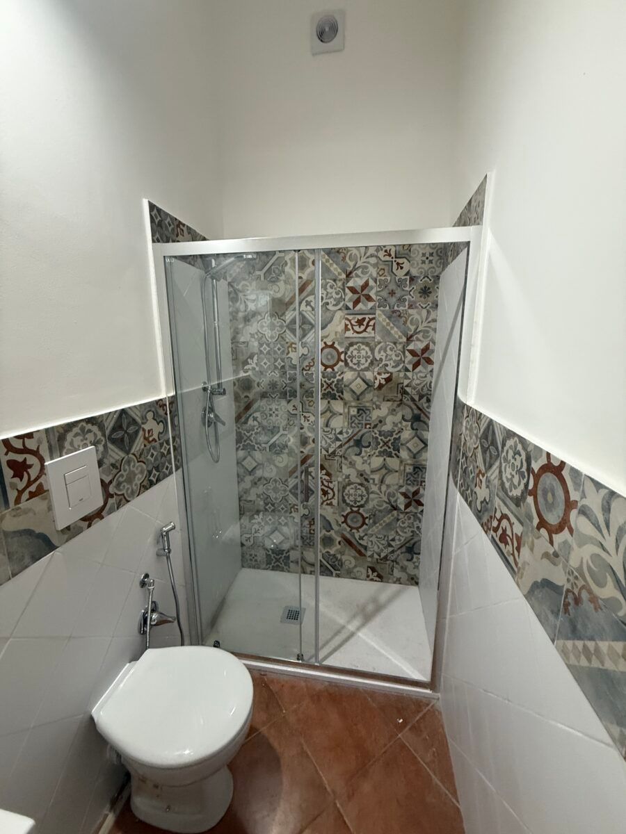 Piccolo bagno con doccia in vetro, piastrelle a motivi e WC.