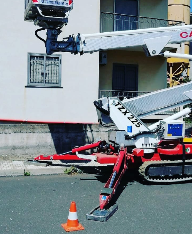 Una piattaforma aerea rossa e bianca con un braccio esteso, posizionata su una strada accanto a un edificio.