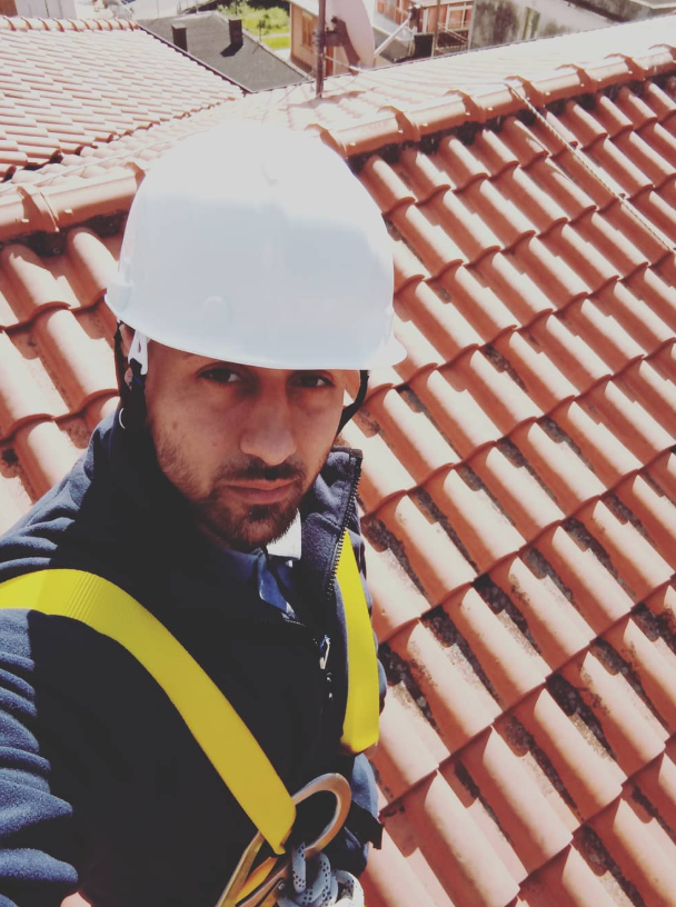 Uomo con casco e imbracatura di sicurezza su un tetto di tegole.