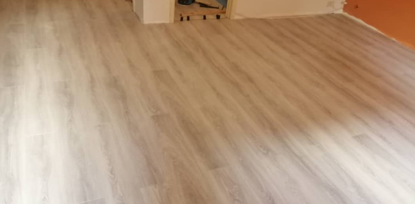 Pavimento effetto legno in una stanza con pareti chiare e un angolo dipinto di arancione.