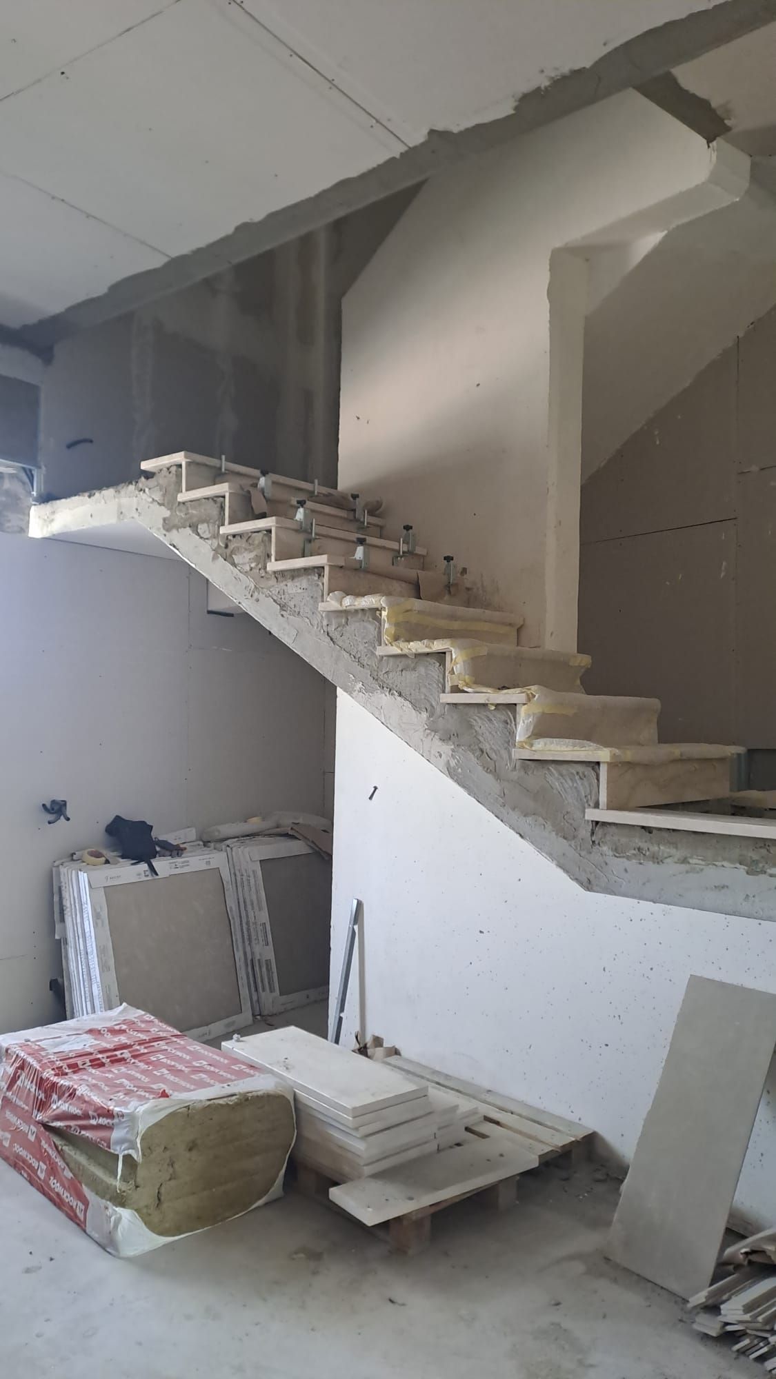 Scala in costruzione con gradini in cemento e pareti grezze all'interno di un edificio.
