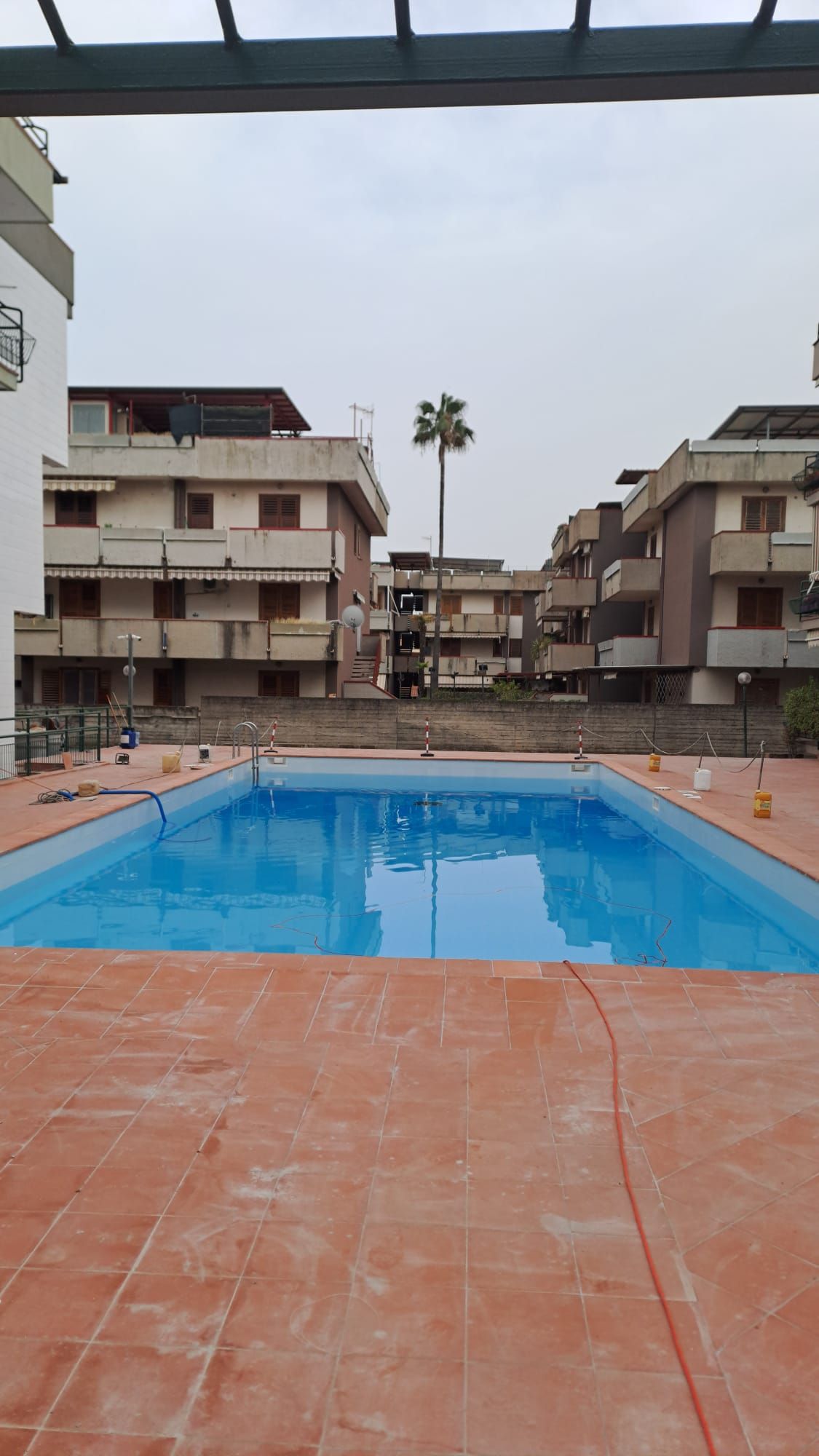 Piscina all'aperto in un cortile, circondata da condomini sotto un cielo nuvoloso.