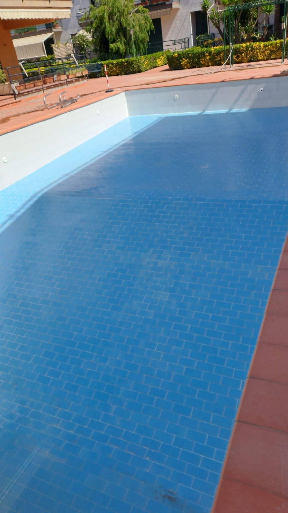 Piscina esterna vuota con interno piastrellato blu e bordi rivestiti in mattoni.