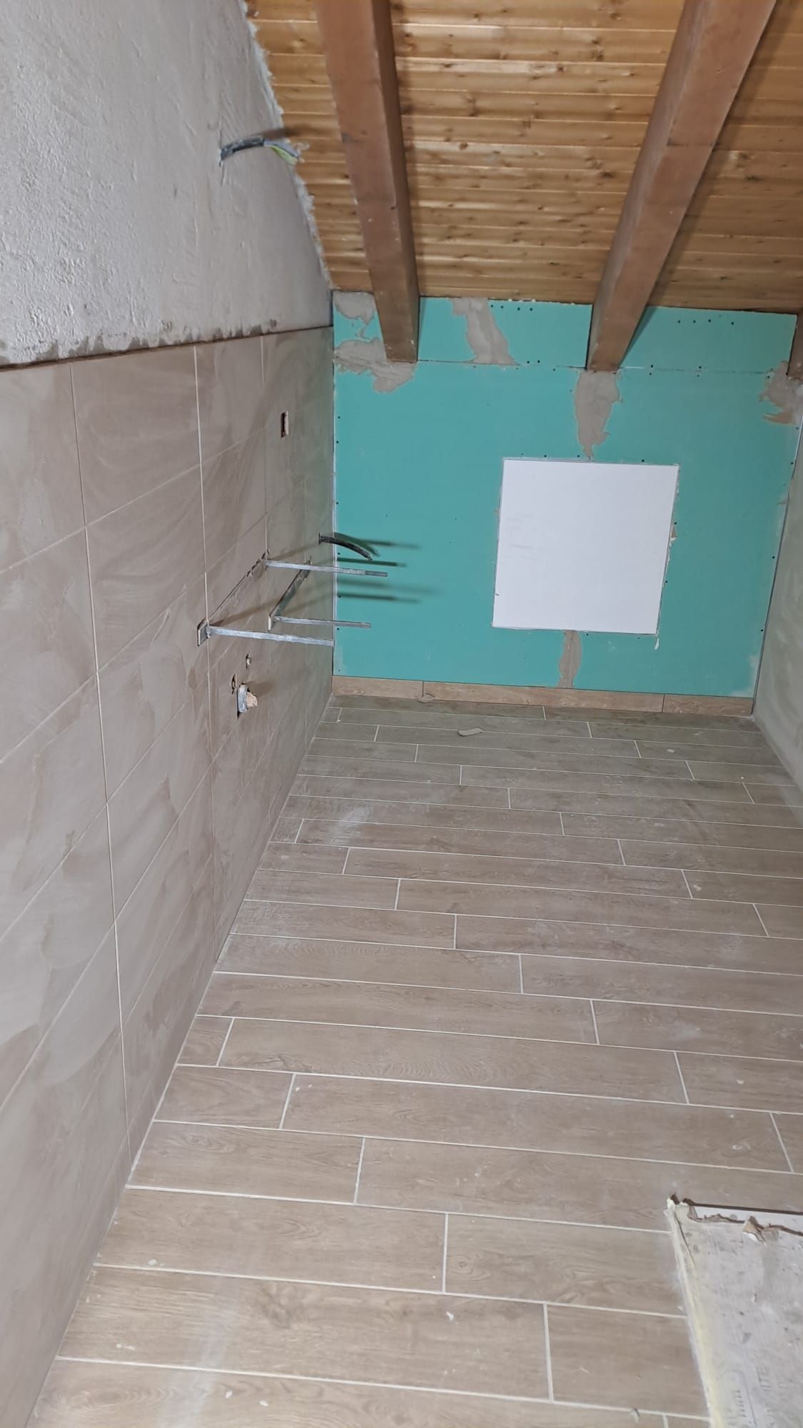 Stanza interna in costruzione con pavimento e parete piastrellati, travi a vista e cartongesso grezzo.