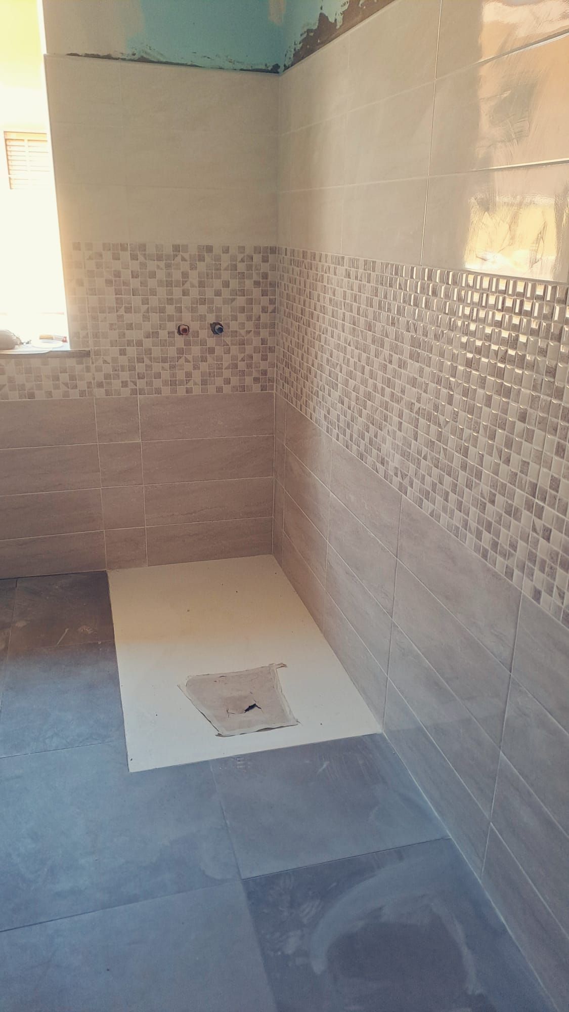 Bagno in costruzione con pareti piastrellate, piastrelle beige e dettagli decorativi in ​​mosaico.
