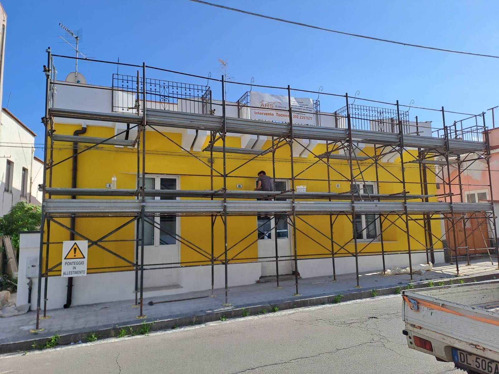 Edificio giallo in fase di ristrutturazione con impalcature; una persona sta lavorando.