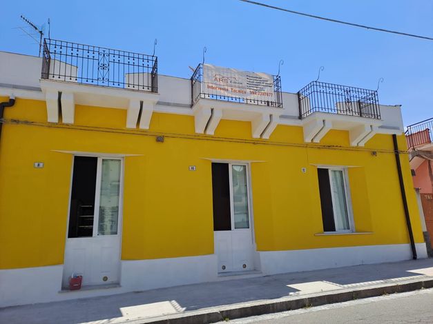 Edificio giallo con balconi su una strada soleggiata. Rifiniture bianche, finestre aperte e piccole ringhiere dei balconi.