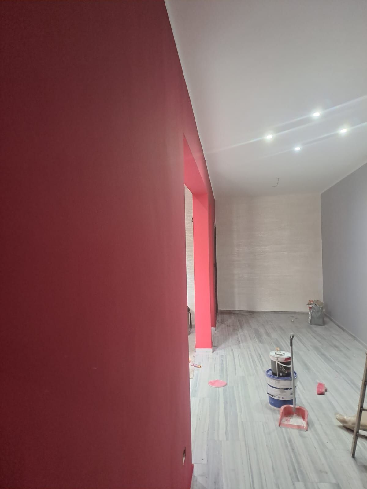 Interno di una stanza in fase di tinteggiatura, con una parete rossa, un soffitto bianco e pareti grigie.