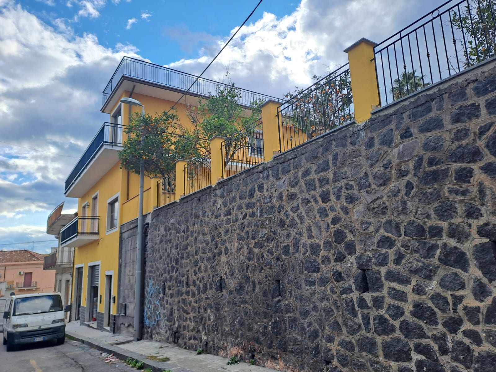Edificio giallo dietro un muro di pietra scura in una strada con cielo nuvoloso.