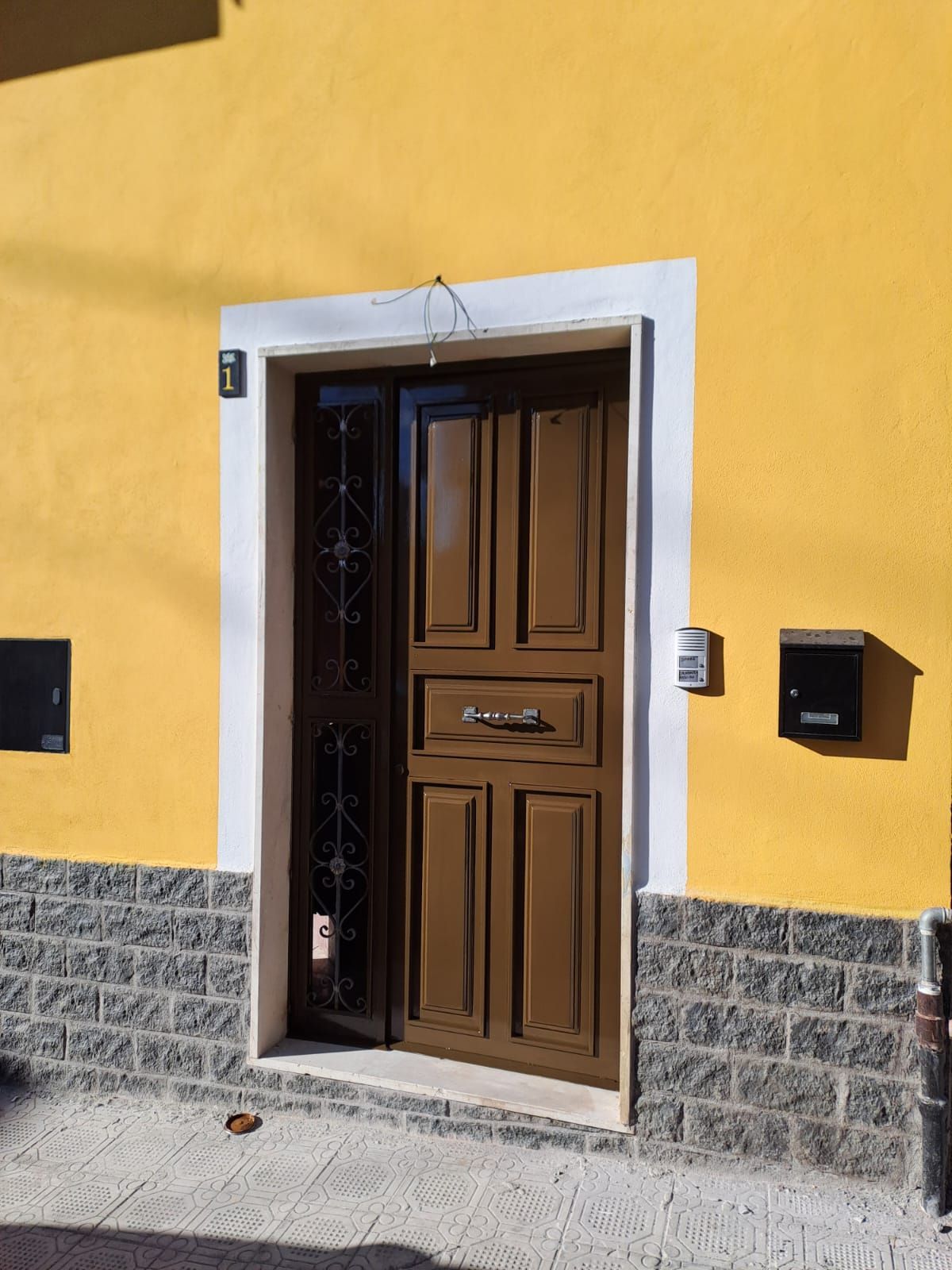 Porta marrone con schermo decorativo, inserita in un vano con cornice bianca contro una parete gialla, con base in mattoni.