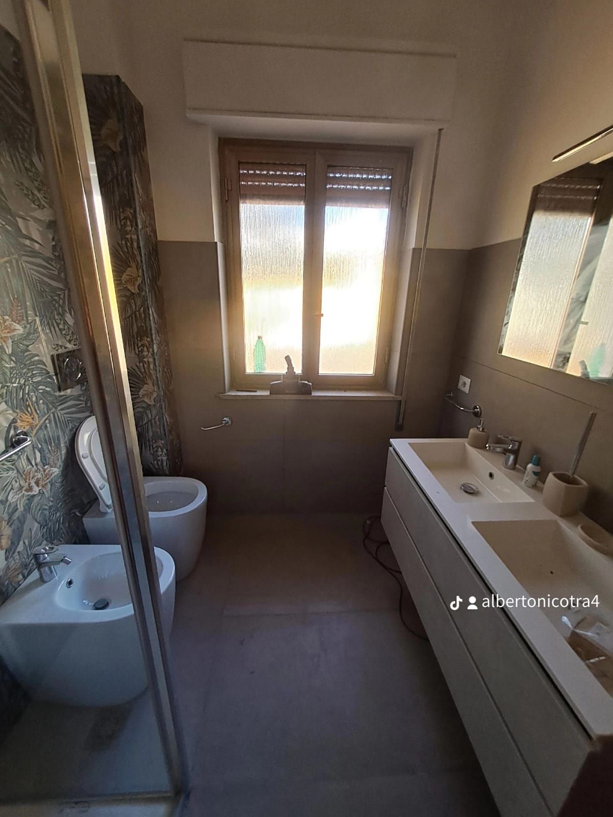 Bagno con lungo mobile lavabo bianco, finestra con persiane, WC e doccia.