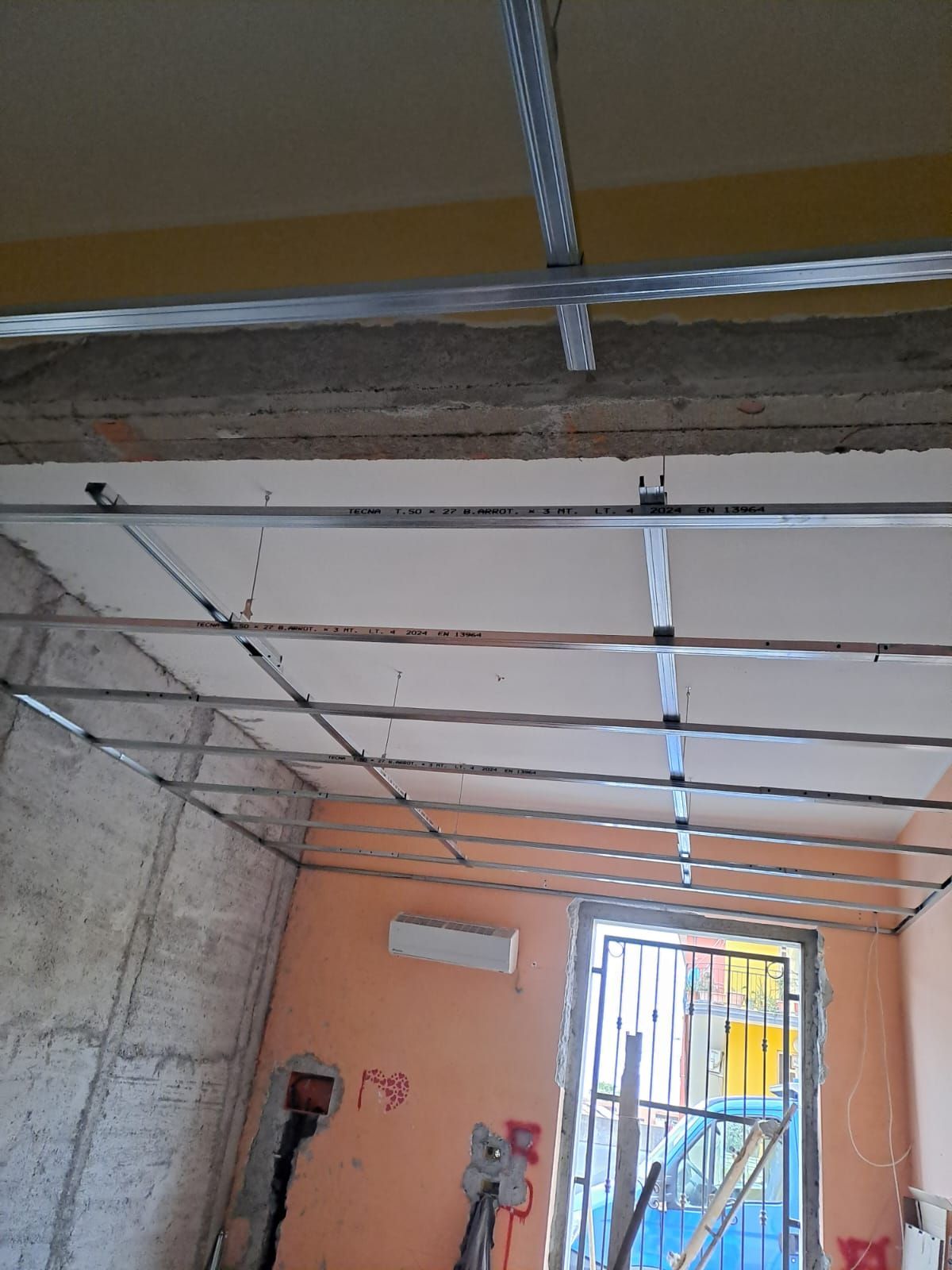 Struttura metallica di un controsoffitto installato in una stanza. Le pareti sono realizzate in un mix di cemento e intonaco verniciato.