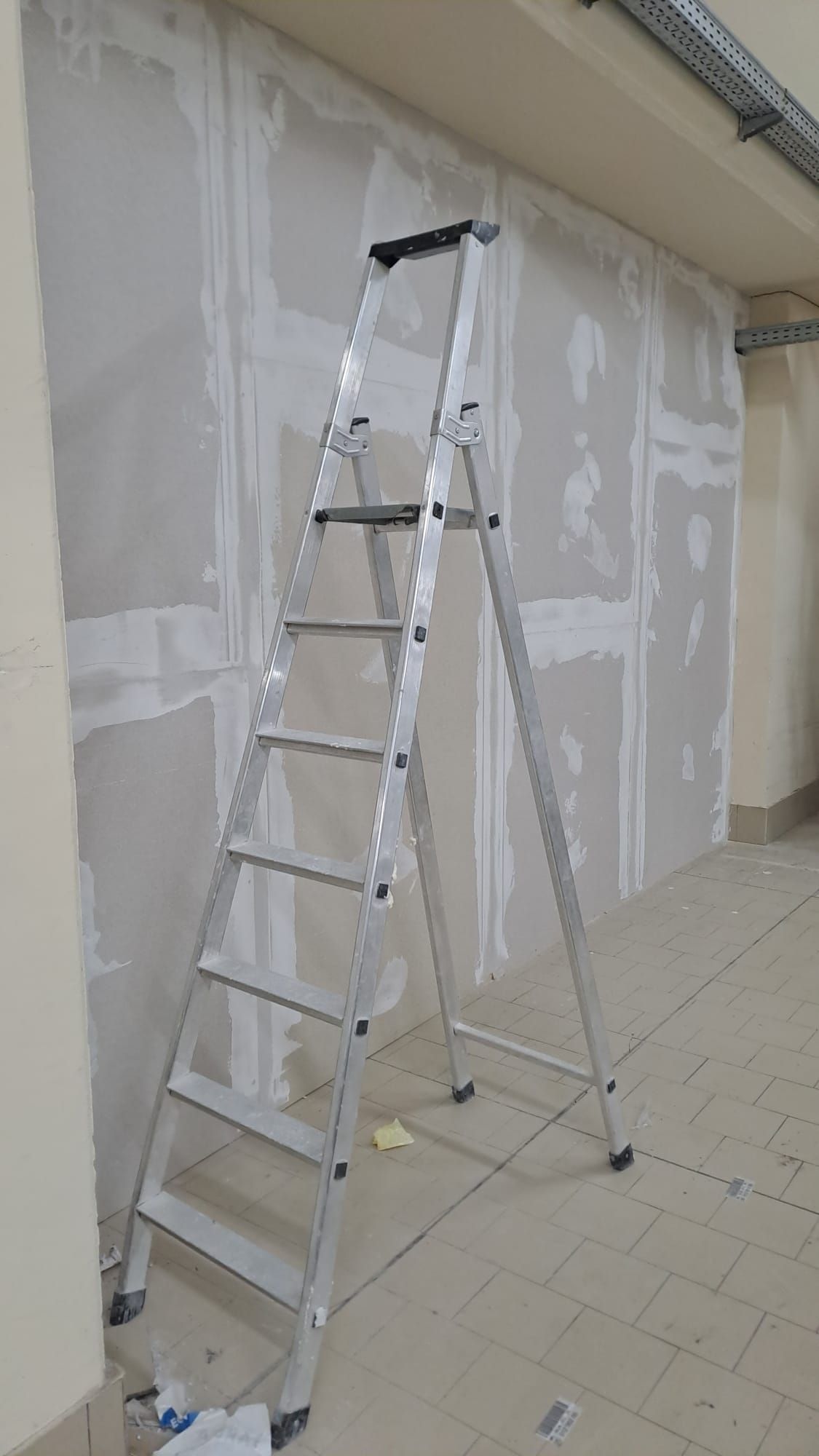 Scala a pioli in alluminio appoggiata al muro a secco in una stanza in costruzione.