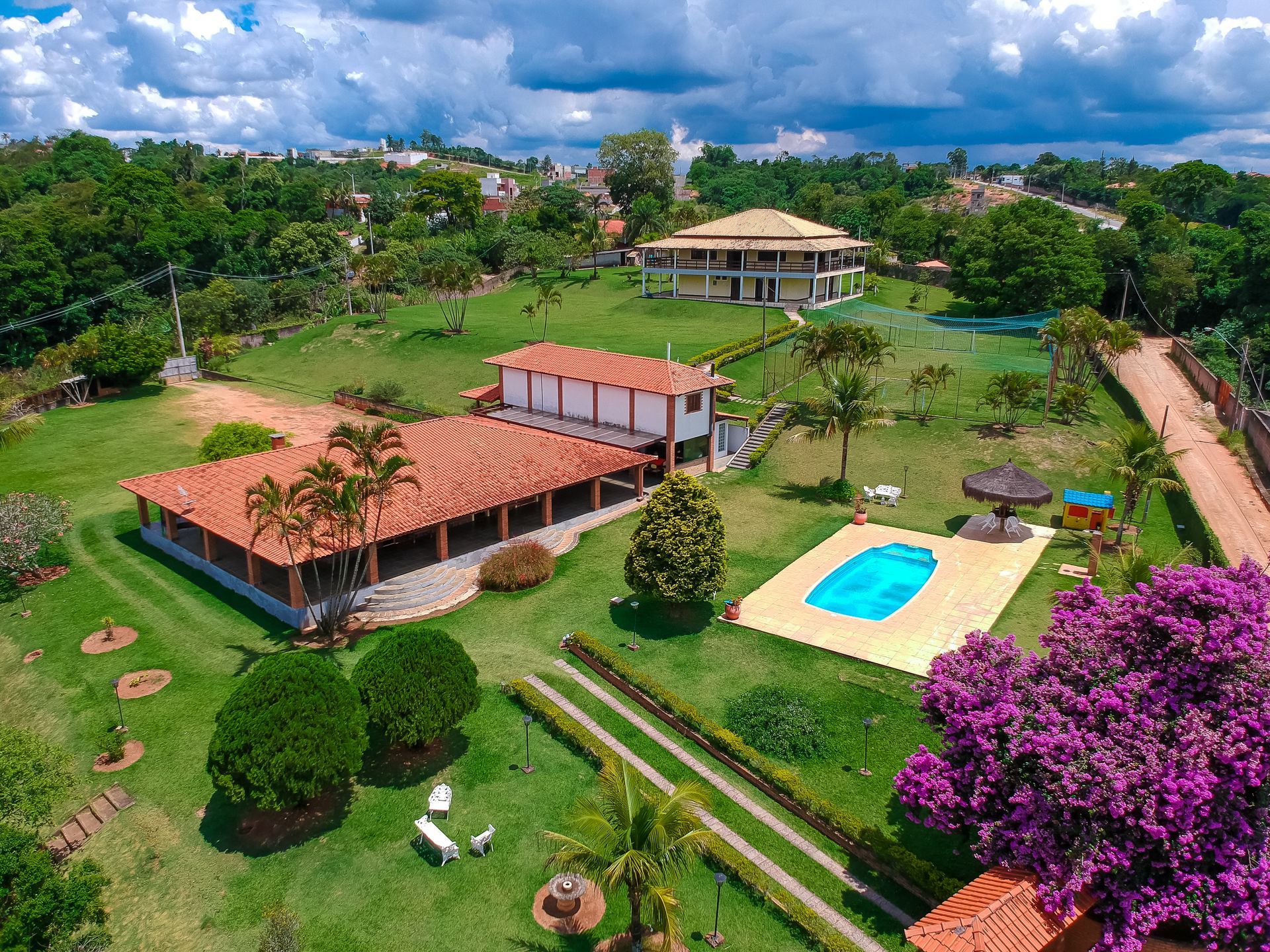 Vista aérea de um resort tropical com edifícios de telhados vermelhos, gramados verdes, piscina e árvores.