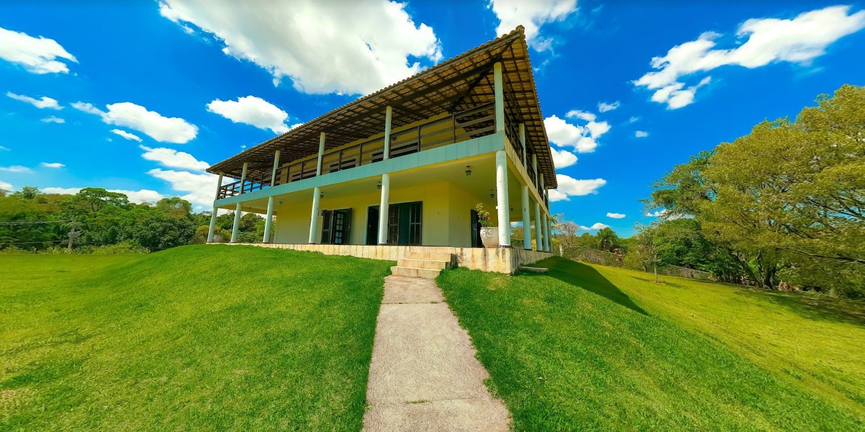 Casa moderna com laterais abertas em uma colina gramada sob um céu azul brilhante com nuvens.