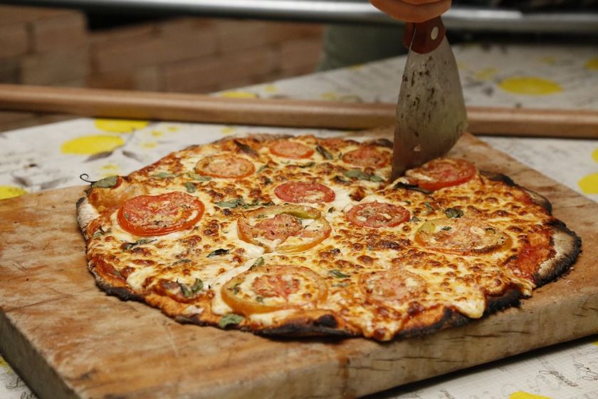 Pizza sendo fatiada em uma tábua de madeira com um cortador de metal.