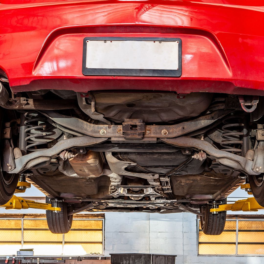 the underside of a red car on a lift in a garage .