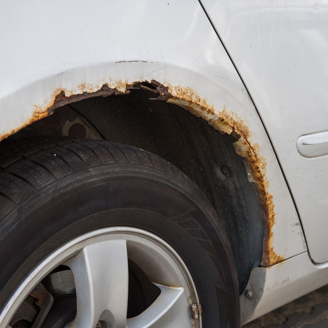 a white car with rust on the fender and tire