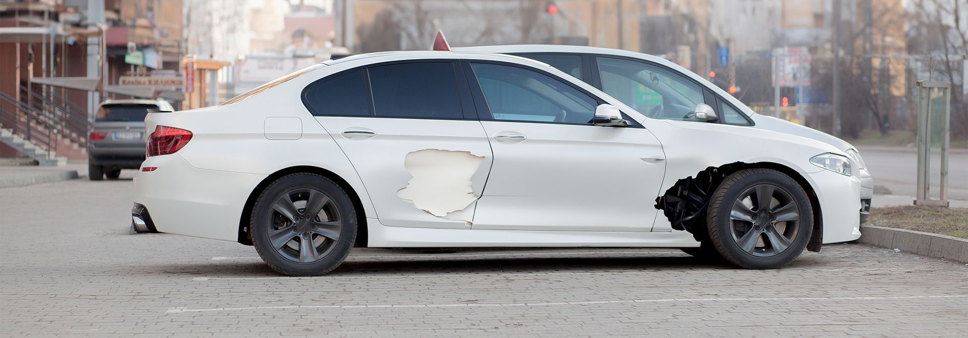 a white car with a hole in the door is parked on the side of the road .