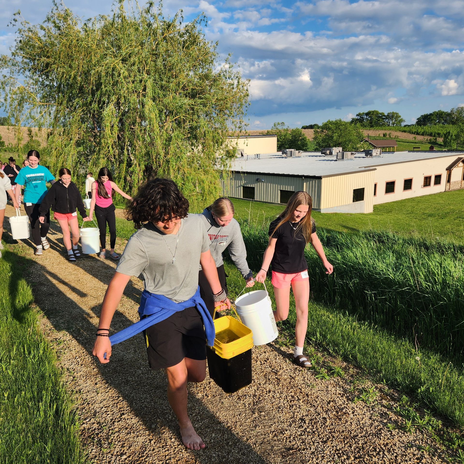 A group of people are walking down a gravel path carrying buckets