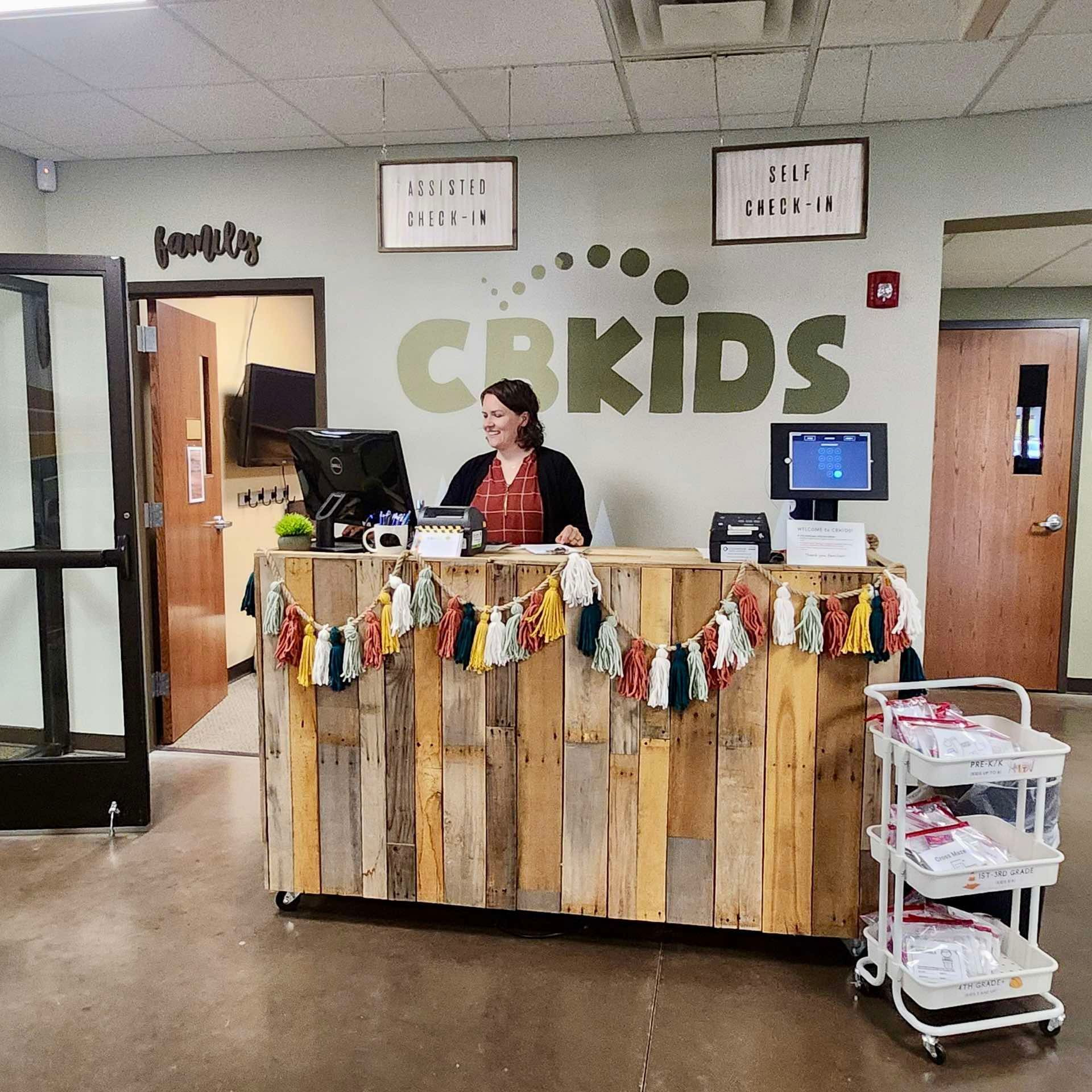 A woman sits at a counter in front of a wall that says cbkids