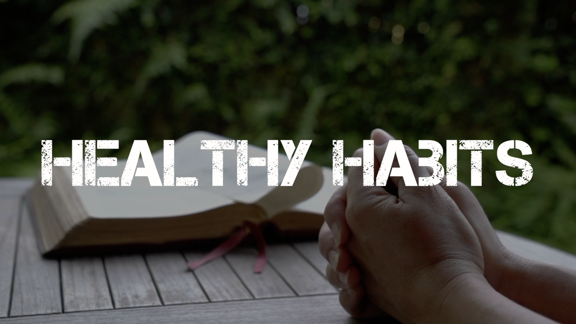 A person is praying with their hands folded in front of a bible.