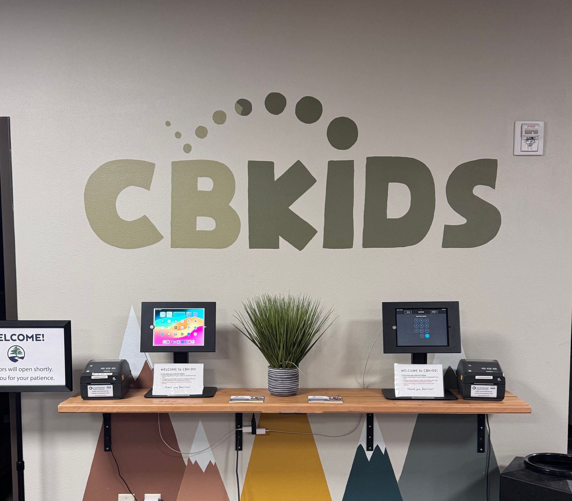A woman sits at a counter in front of a wall that says cbkids