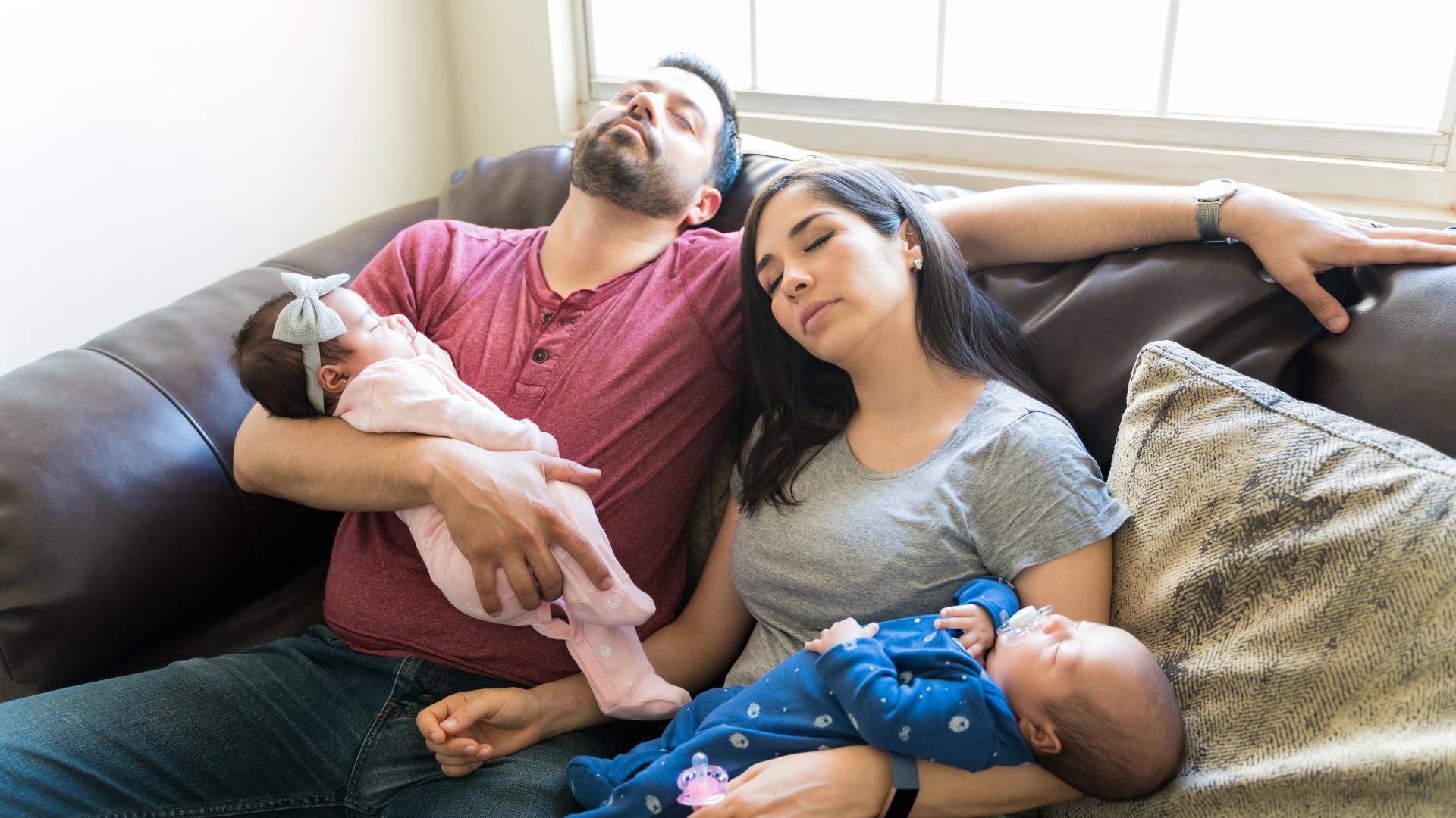 A man and woman are laying on a couch holding two babies.