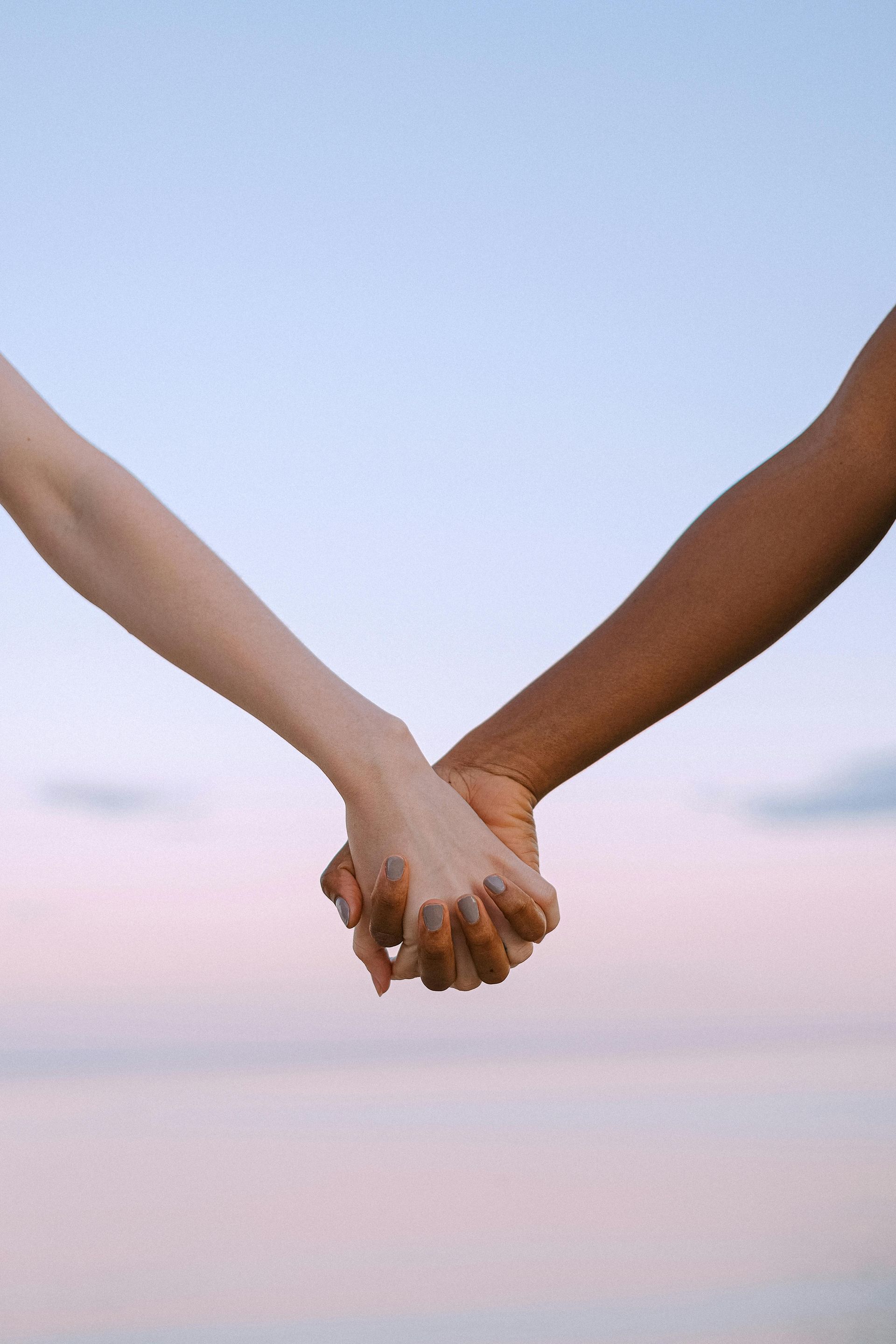 Two people are holding hands in front of a body of water.