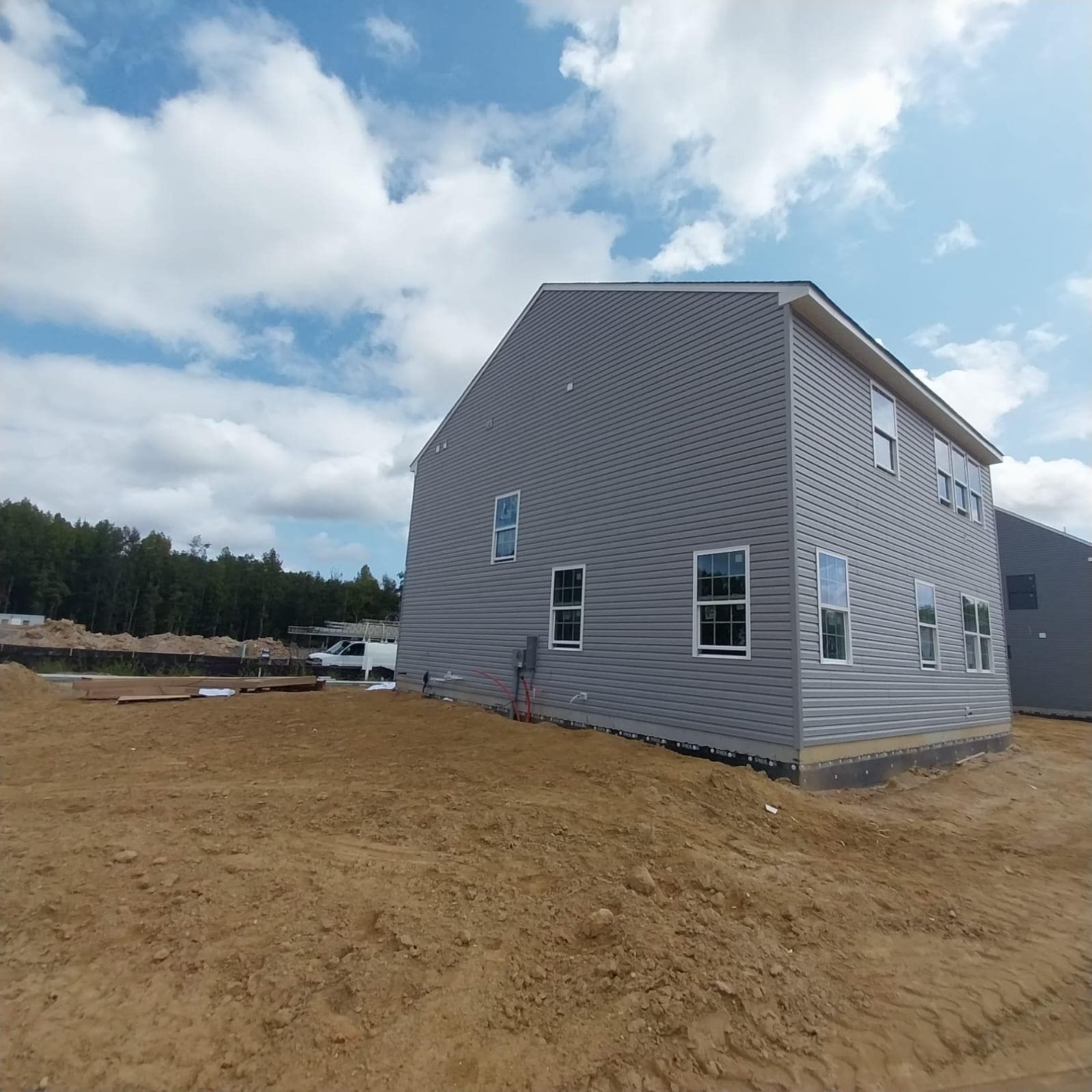 Gray two-story house under construction against a partly cloudy sky. Brown dirt and construction site in the foreground.