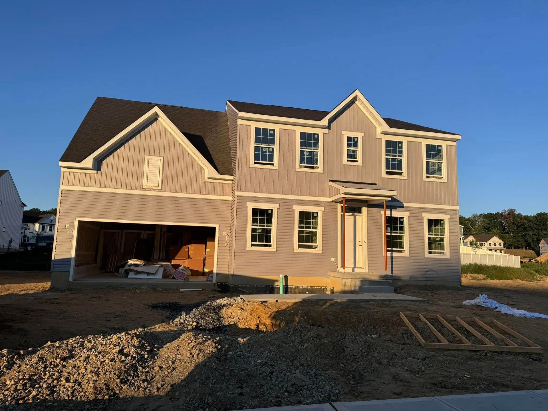 New two-story house under construction with a garage. Gray siding, white window frames, on a sunny day.