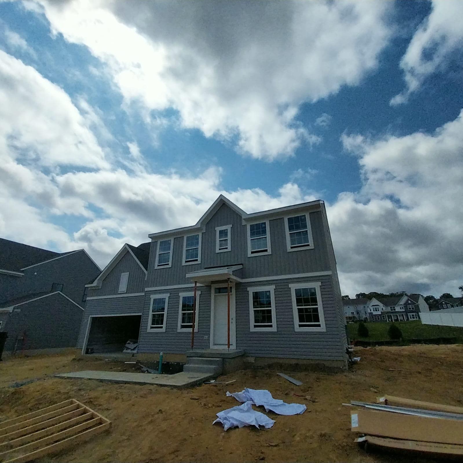 Two-story house under construction with gray siding against a cloudy blue sky.