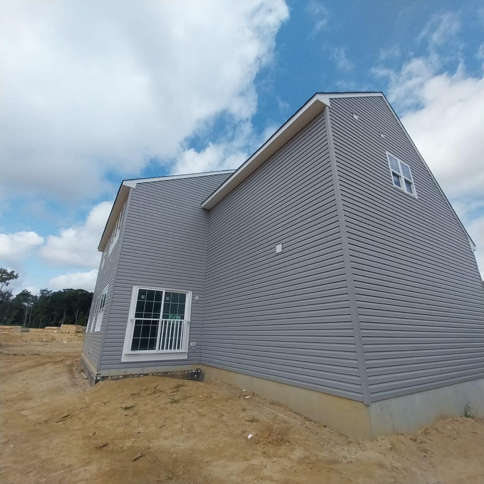 Gray sided house under construction with white windows, against a blue sky with clouds.