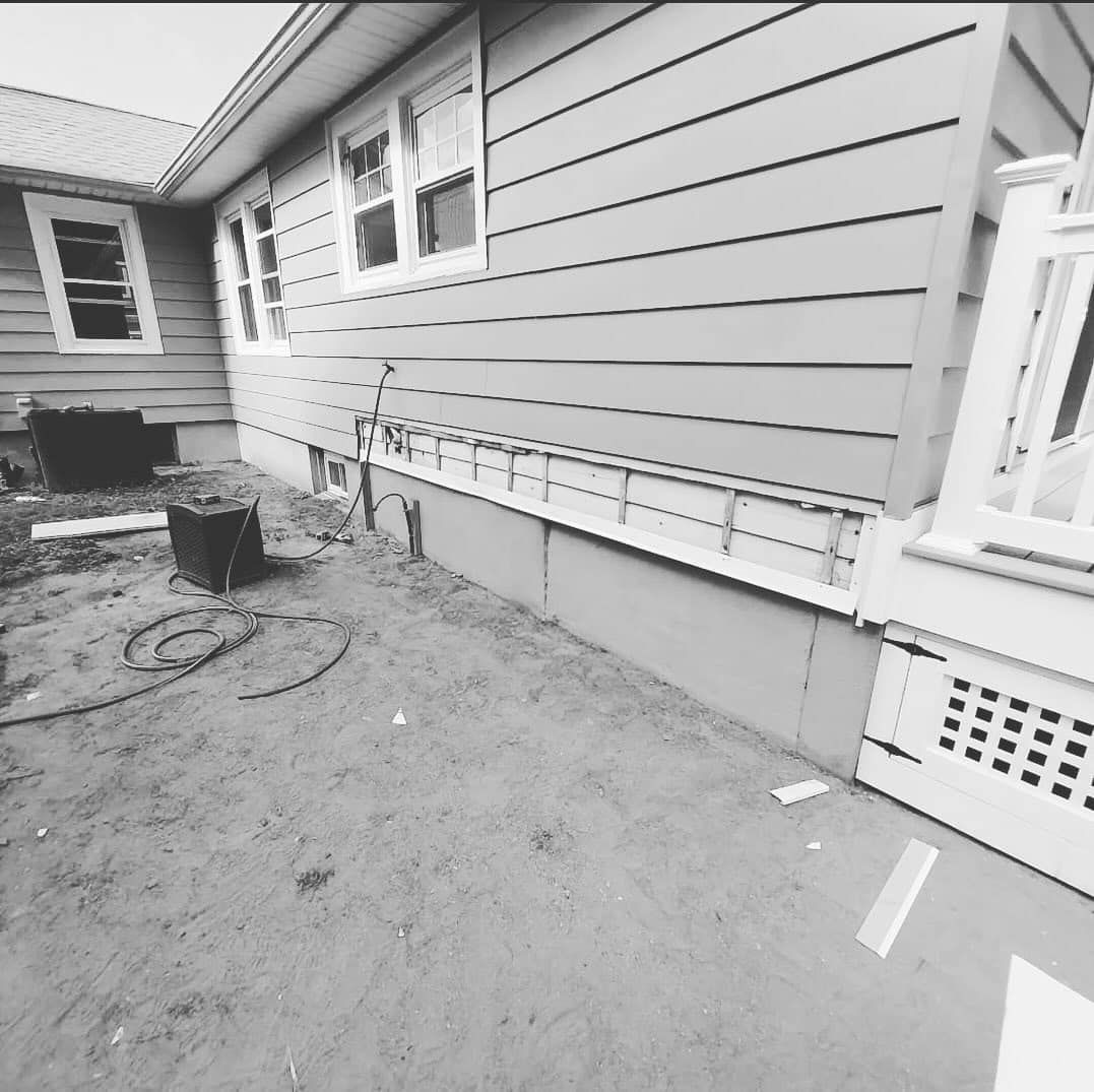 Black and white photo of a house exterior with siding, windows, and a deck.